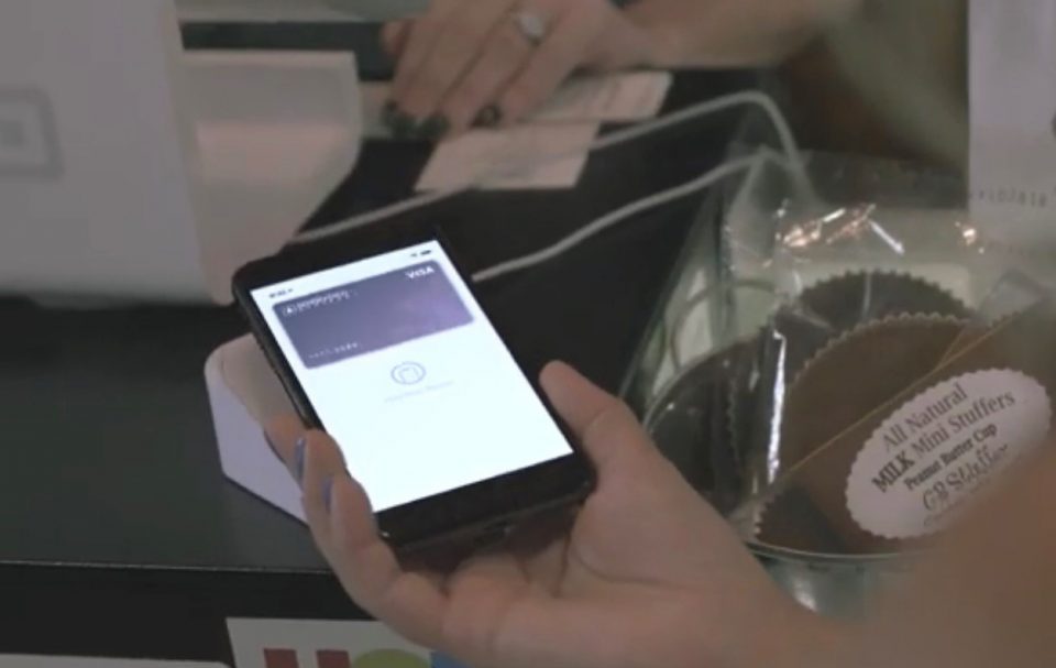Person holding smartphone over contactless payment reader with image of Biddeford Savings debit card on the phone screen